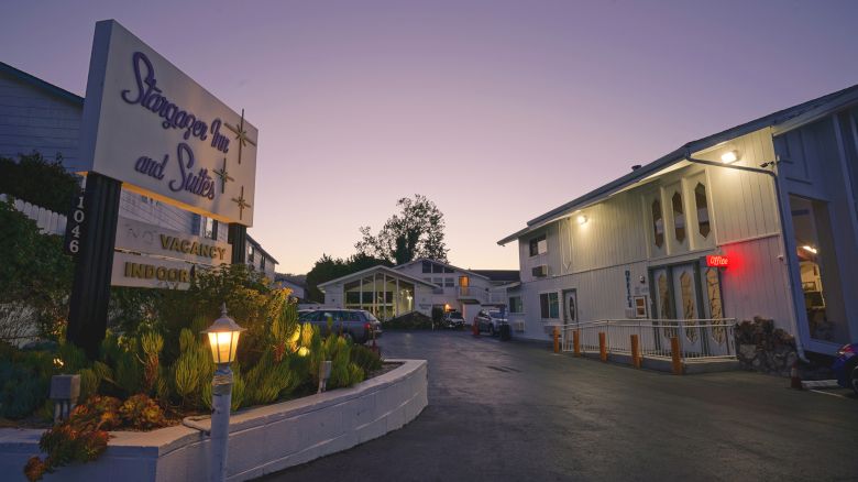 A small motel at dusk with a sign, courtyard, and two- to three-story buildings, dim streetlights, and a quiet, empty driveway.